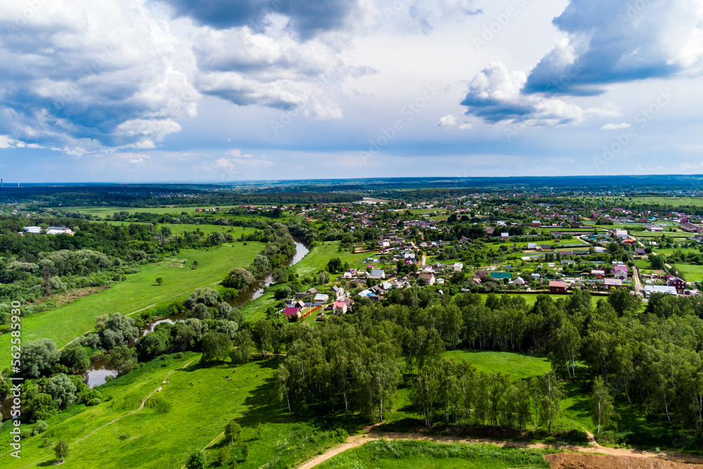 Panoramic aerial view of a rural landscape with green fields, a flowing river and a village