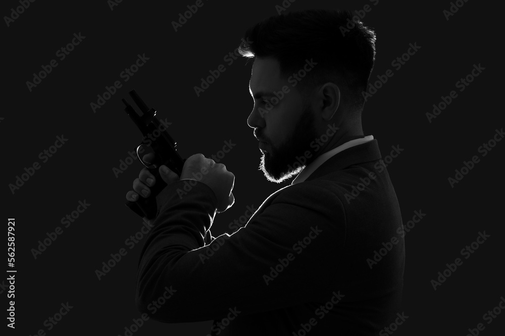 Silhouette of young man in suit with gun on dark background Silhouette of young man in suit with gun on dark background