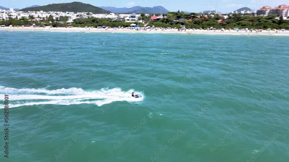 Drone aerial scene of person riding jet ski doing water sports on beach near sand with blue sea in Jurere Internacional Drone aerial scene of person riding jet ski doing water sports on beach near sand with blue sea in Jurere Internacional
