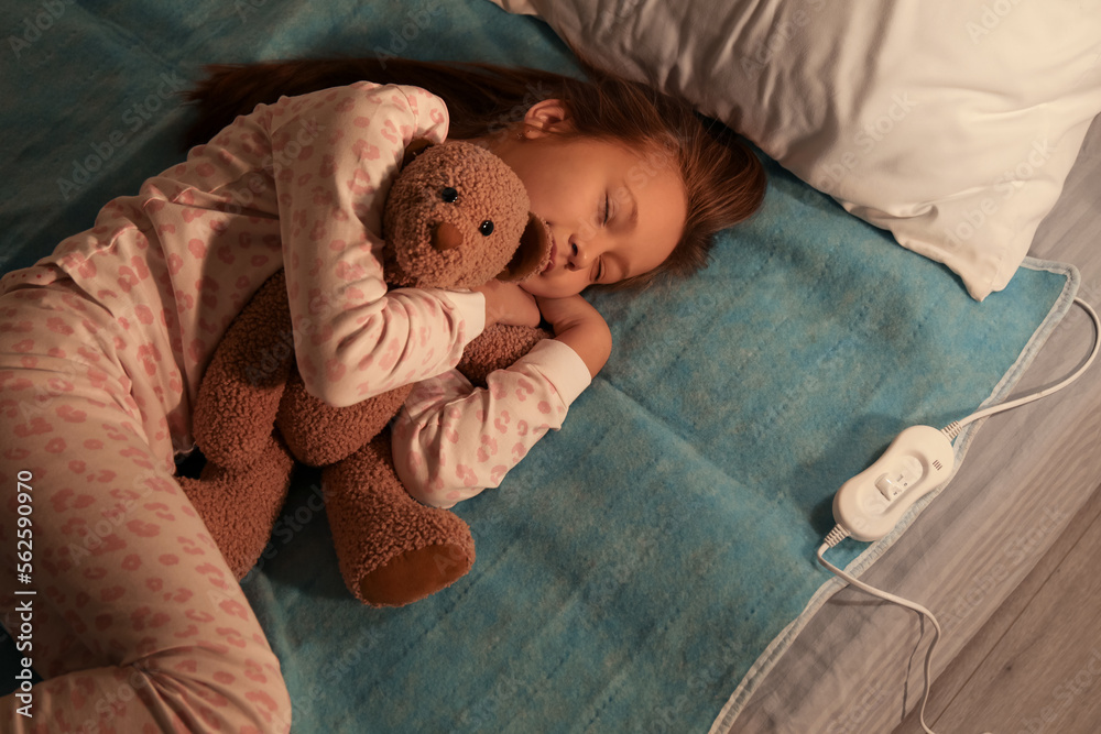 Little girl with toy sleeping on electric heating pad in bedroom at