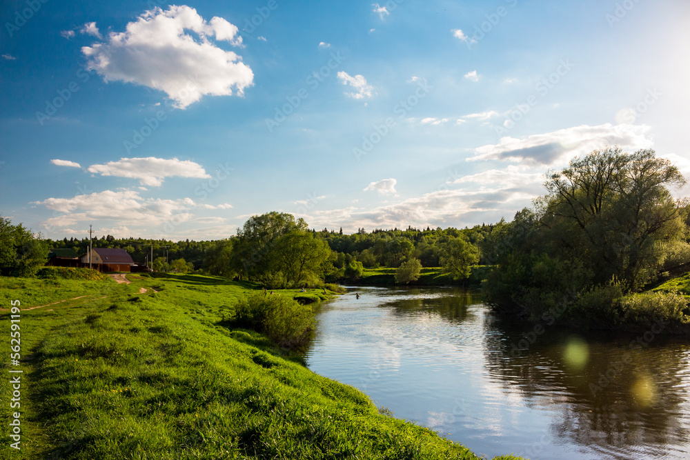 Picturesque pastoral landscape with a view of a river in the countryside, houses and bathers in the background