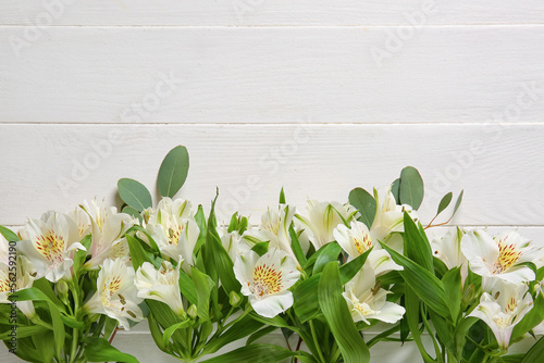 Composition with beautiful alstroemeria flowers and eucalyptus branches on light wooden background