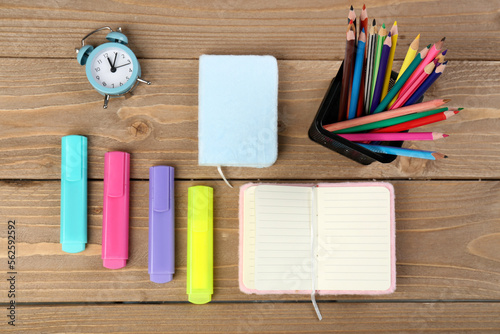 Pencils holder, markers, notebooks and clock on wooden background