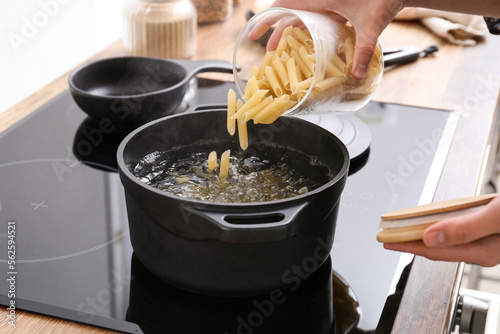 Woman pouring raw pasta into pot with boiling water on stove photo