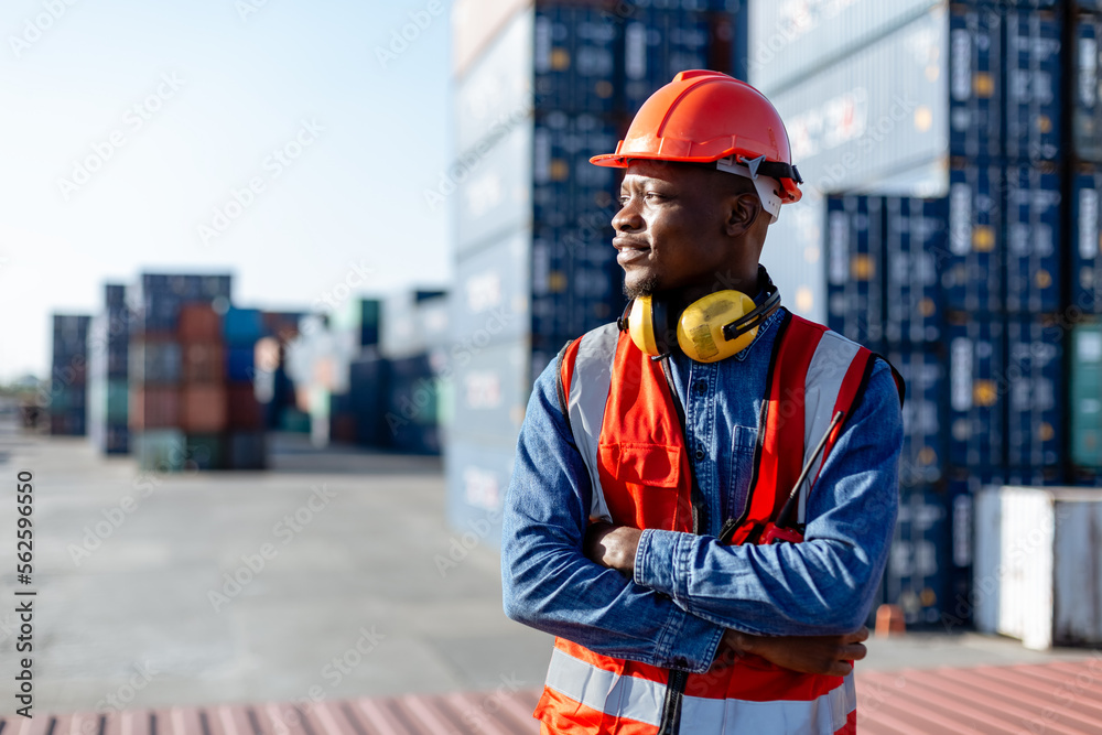 Black male African American smiling engineering in uniform wear hard hat standing containers yard. Area logistics import export and shipping. - obrazy, fototapety, plakaty 