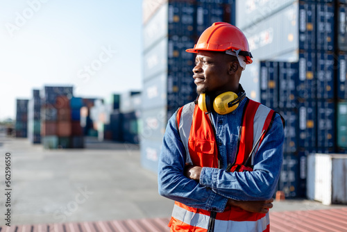 Fototapeta Black male African American smiling engineering in uniform wear hard hat standing containers yard
