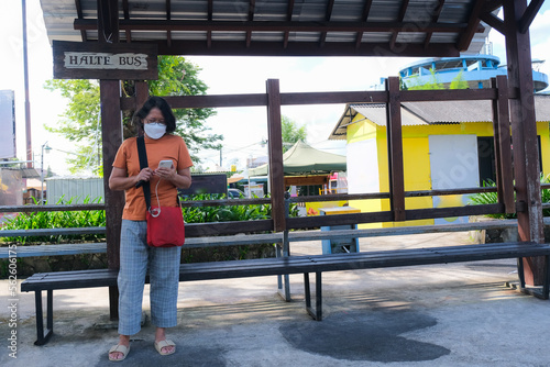 Woman standing alone at a bus stop waiting for her public transporation © Simon