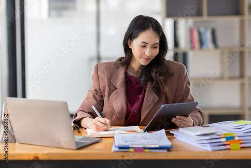 Freelancer Happy business Asian woman in knitwear taking notes at laptop sitting at desk office, finance concept. 