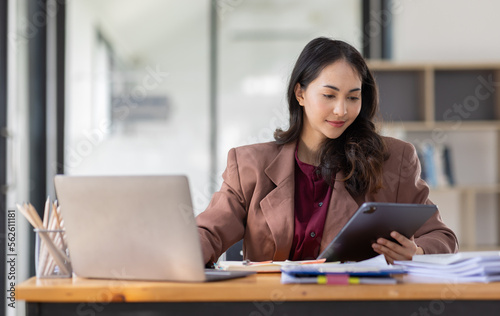 Freelancer Happy business Asian woman in knitwear taking notes at laptop sitting at desk office, finance concept. 