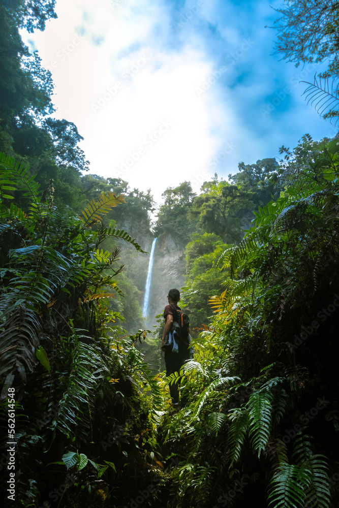 young hiker admiring a mountain waterfall surrounded by vegetation in the middle of the tropical jungle of Costa Rica