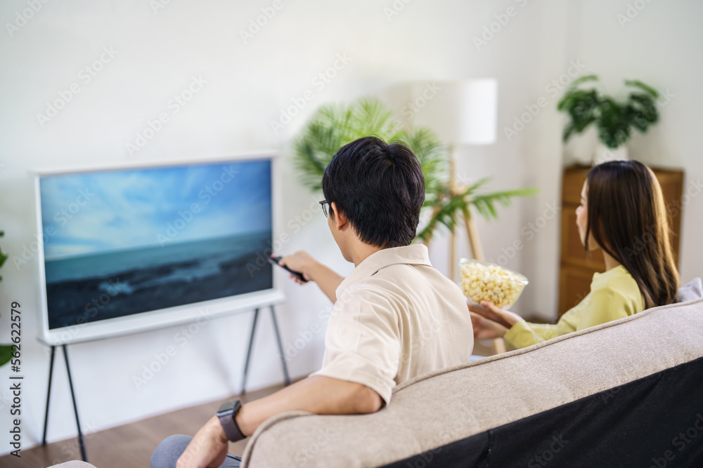 Asian family Watching smart TV together and using remote controller Hand holding popcorn at home with the remote control movie or TV series spending time at home Asian family Watching smart TV together and using remote controller Hand holding popcorn at home with the remote control movie or TV series spending time at home