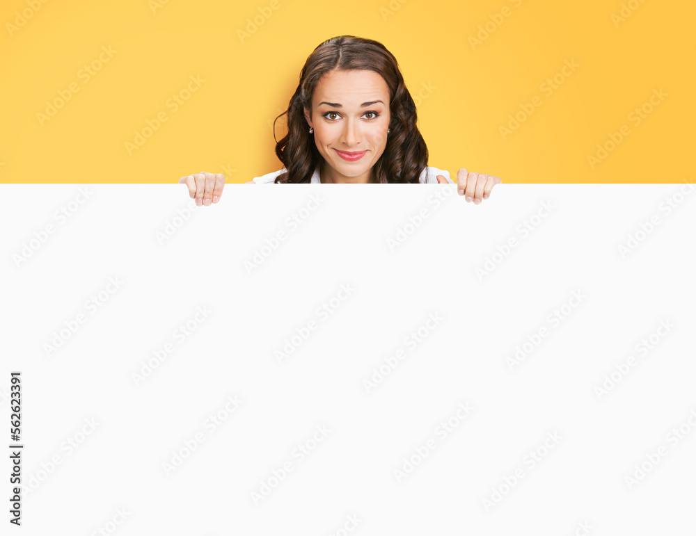 Smiling business woman standing beehind, peeping out white empty mock up signboard. Success and advertising concept. Copy space place, isolated on yellow background. Young businesswoman. Smiling business woman standing beehind, peeping out white empty mock up signboard. Success and advertising concept. Copy space place, isolated on yellow background. Young businesswoman.