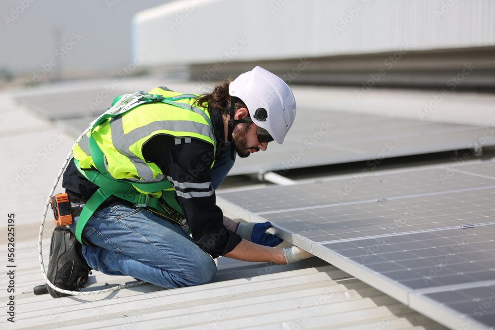 A worker is fixing solar panels on the roof. Engineer and technician using laptop checking and operating solar panels system on rooftop of solar cell farm power plant, Renewable energy source. A worker is fixing solar panels on the roof. Engineer and technician using laptop checking and operating solar panels system on rooftop of solar cell farm power plant, Renewable energy source.