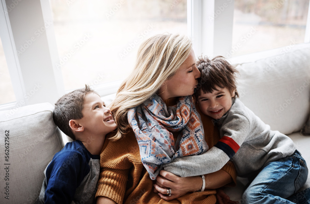 Happy family, hug and kiss from mother to children while together on living room sofa at the house. Woman and kids in lounge for love, care and safety while bonding to relax and spend time at. home Happy family, hug and kiss from mother to children while together on living room sofa at the house. Woman and kids in lounge for love, care and safety while bonding to relax and spend time at. home