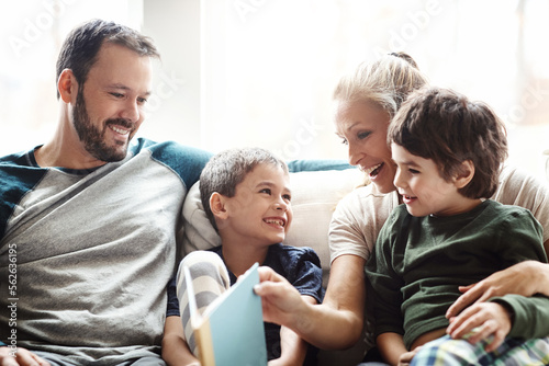 Mother, father and kids on sofa for storytelling time in living room of happy family home. Love, books and couple with children smile, book and fantasy story time on couch, growth and development.