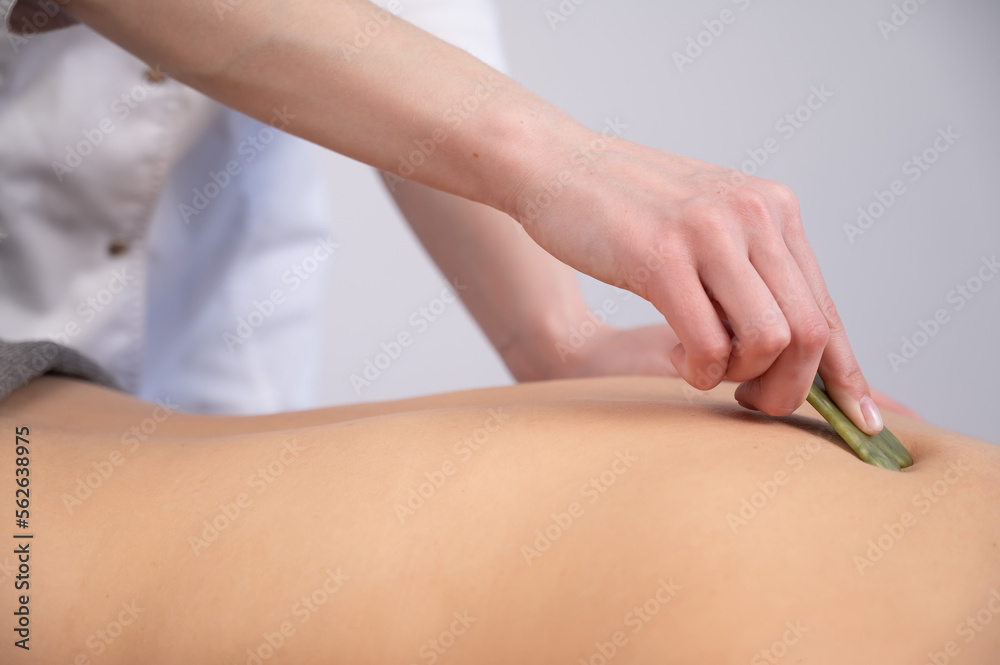 The masseur makes a back massage with a gouache scraper to a female client. 