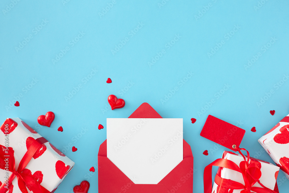 Valentine's Day presents concept. Flat lay photo of open red envelope with white card, gift boxes and red hearts on blue background with copy space. Holiday card idea. Valentine's Day presents concept. Flat lay photo of open red envelope with white card, gift boxes and red hearts on blue background with copy space. Holiday card idea.