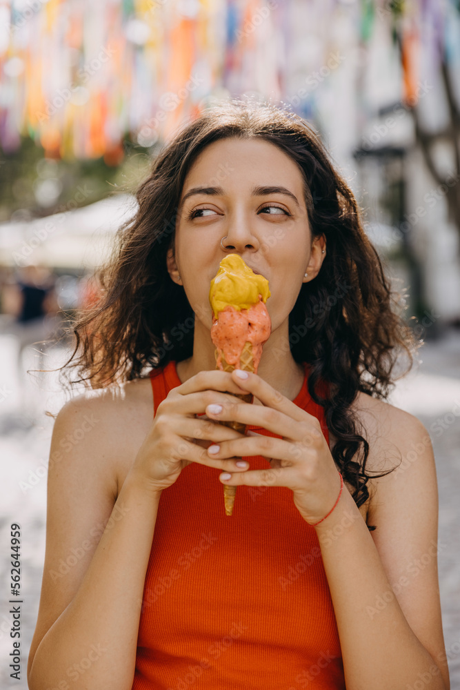 Happy young brunette woman on city street on a hot summer day, eating a big double layered ice cream. Happy young brunette woman on city street on a hot summer day, eating a big double layered ice cream.