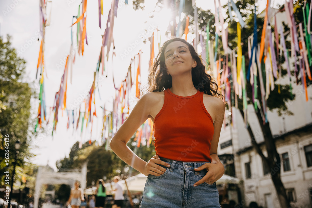 Young happy woman with curly brunette hair, smiling, walking on city streets on hot summer day. Young happy woman with curly brunette hair, smiling, walking on city streets on hot summer day.