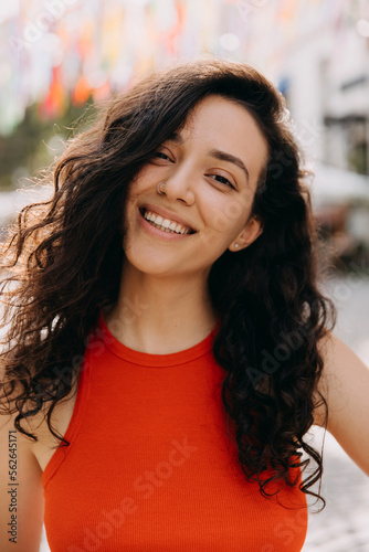 Closeup portrait of a young woman with curly brunette hair, happy, with beautiful smile, looking at camera. © Bostan Natalia