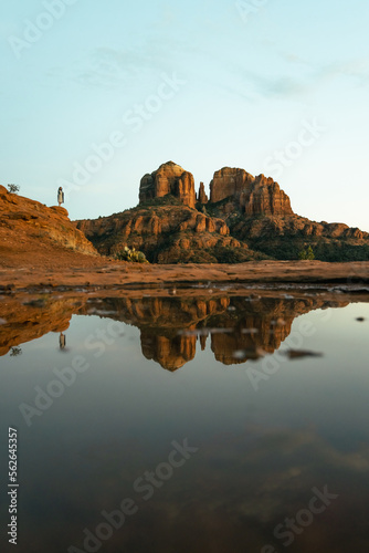Young beautiful woman standing on rock point looking out at Cathedral Rock in Sedona Arizona USA Southwest at sunset with reflection from small pool.