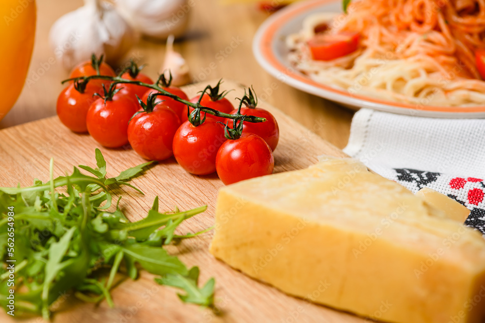 Sprig of cherry tomatoes on the table with garlic, parmesan cheese, arugula leaves and a bowl of pasta. Sprig of cherry tomatoes on the table with garlic, parmesan cheese, arugula leaves and a bowl of pasta.
