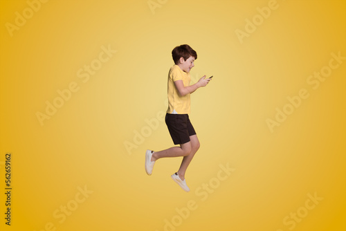 Full body little small boy wearing yellow t-shirt holding mobile cell phone isolated on yellow background studio.