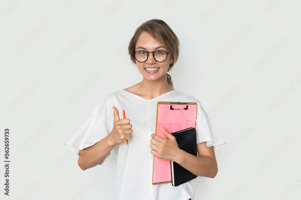 Positive smiling student woman wearing eyeglasses showing thumb up, likes an idea, holding books, isolated over white background Positive smiling student woman wearing eyeglasses showing thumb up, likes an idea, holding books, isolated over white background