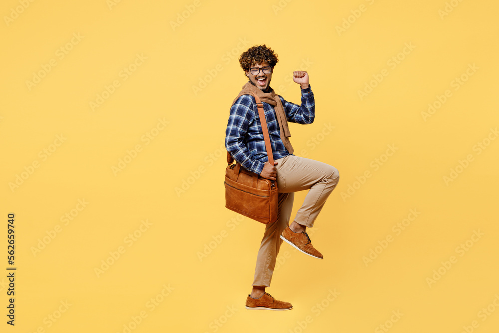 Full body side view young teacher successful teen Indian boy IT student wear casual clothes shirt glasses bag do winner gesture isolated on plain yellow color background High school university concept - obrazy, fototapety, plakaty 