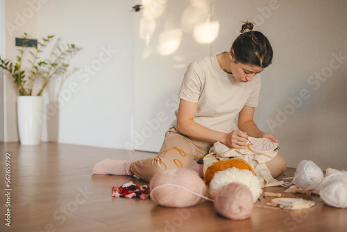 Young beautiful woman is engaged in embroidering on the embroidery frame sitting on the floor at home. A great picture for a hobby