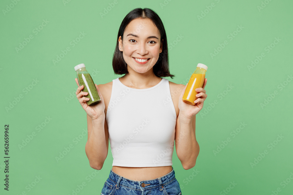 Young woman wear white clothes hold pressed juice yellow vegetable smoothie as detox diet isolated on plain pastel light green background. Proper nutrition healthy fast food unhealthy choice concept. Young woman wear white clothes hold pressed juice yellow vegetable smoothie as detox diet isolated on plain pastel light green background. Proper nutrition healthy fast food unhealthy choice concept.