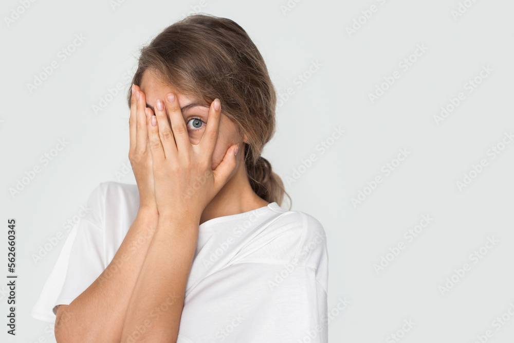 Frightened caucasian woman covering face with palms, peeking through fingers at something isolated over white background with copy space. Frightened caucasian woman covering face with palms, peeking through fingers at something isolated over white background with copy space.