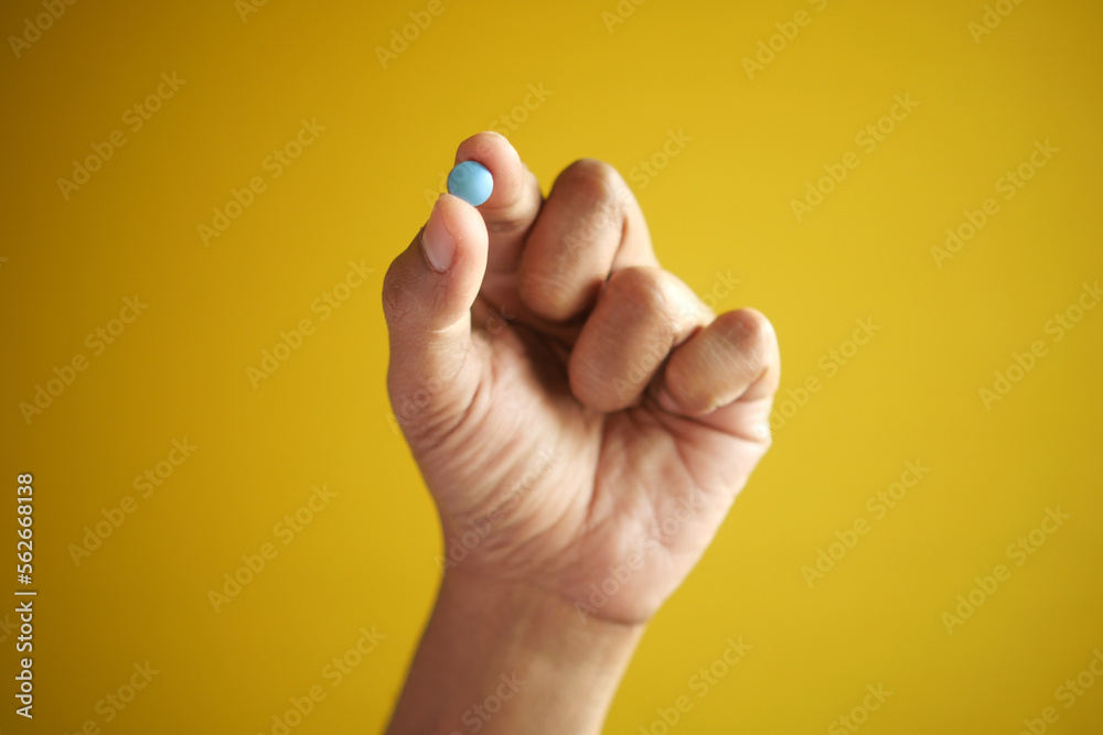 man hand holding a medical pills against yellow background man hand holding a medical pills against yellow background