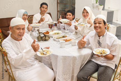 Muslim family holding a plate of special dish while showing thumb up at dining room on Eid celebration moment. 