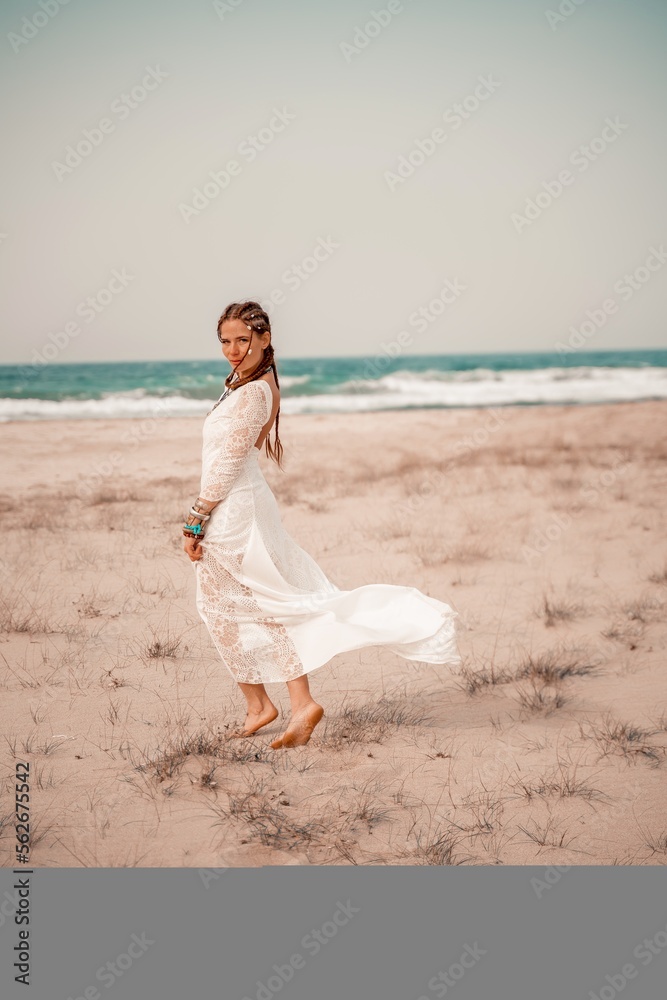 Model in boho style in a white long dress and silver jewelry on the beach. Her hair is braided, and there are many bracelets on her arms. Model in boho style in a white long dress and silver jewelry on the beach. Her hair is braided, and there are many bracelets on her arms.
