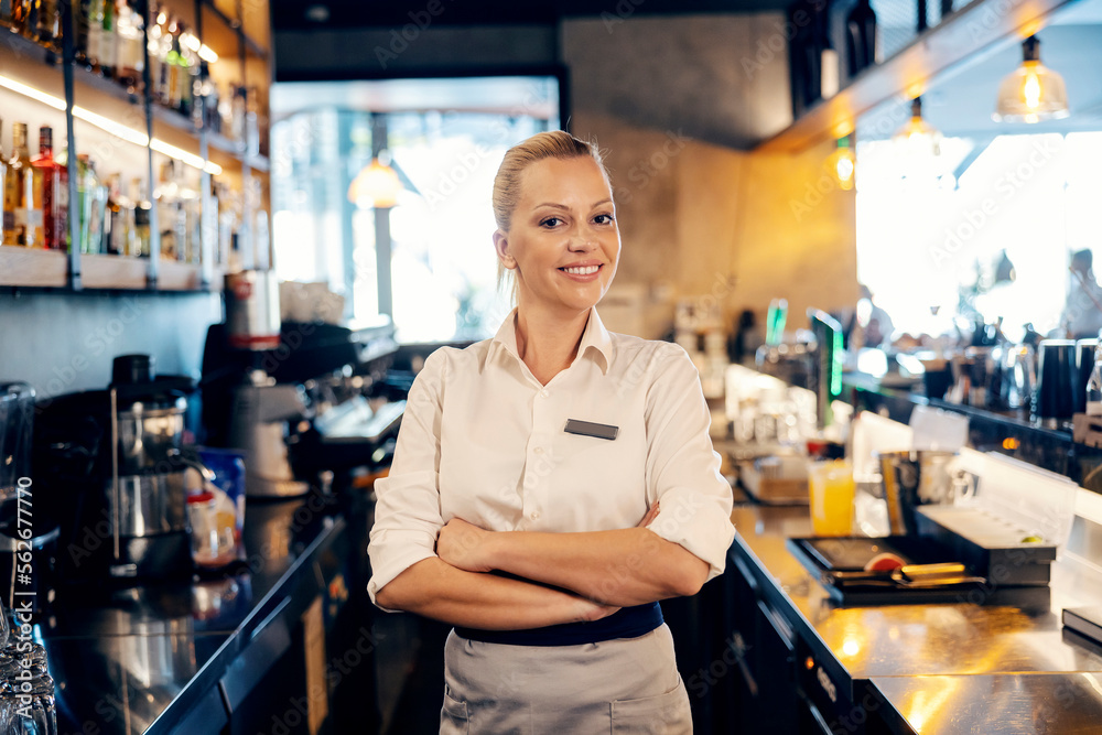 Portrait of a successful bartender standing in a bar and smiling at the camera with arms crossed. Portrait of a successful bartender standing in a bar and smiling at the camera with arms crossed.