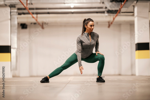 Focused sportswoman is exercising her legs in underground parking lot.