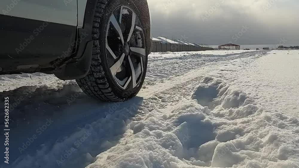 Close-up on the right front wheel of the SUV. A white car is driving through a snowy field. Traveling by car in winter. An exciting road adventure.