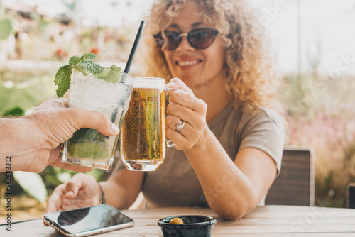 First dating adult couple concept celebration with woman in background toasting and clinking with man out of camera. Happy man and woman at the cafe together enjoying leisure activity with beer mohi photo