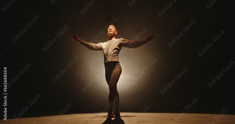 Caucasian male ballet dancer performing on stage, spotted by white light. Young choreographer showing creative performance, isolated on black background 