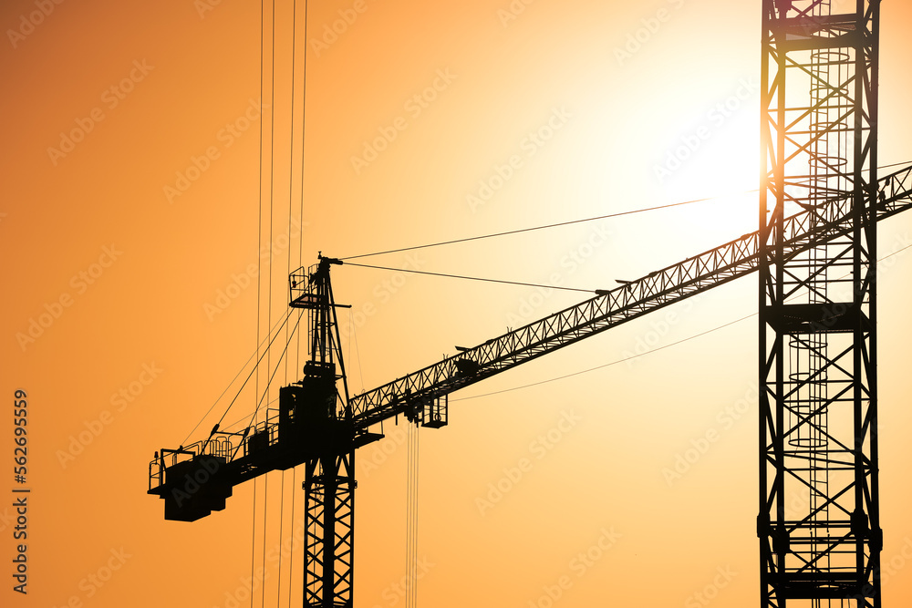 Construction industry concept photo. Construction site with silhouette cranes and sun rising up in background.