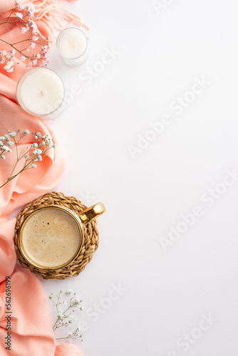 Hello spring concept. Top view vertical photo of cup of frothy coffee on wicker serving mat pink plaid candles and gypsophila flowers on isolated white background with copyspace