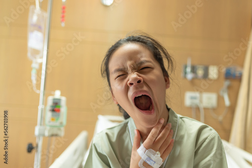 Asian beautiful female patient getting sick and fever, having sore throat and coughing while lying on bed in hospital, teenager sick with saline intravenous, healthcare and health insurance concept.