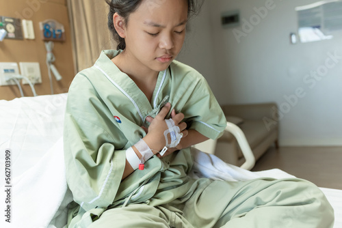 teenager sick and in pain and uses his hands to squeeze his chest chest pain caused by an acute heart attack with IV saline drip to back of hand lying on bed in hospital, medical and health concepts