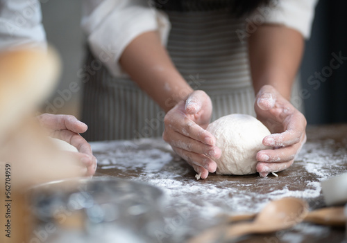 Women chef knead dough in kitchen for fresh homemade cooking, bakery or bread. Female hands thresh flour on table preparing for delicious pizza baking. Happy Asian family making dinner meal together.