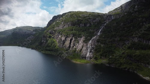 Waterfall flows into a fjord through sun rays