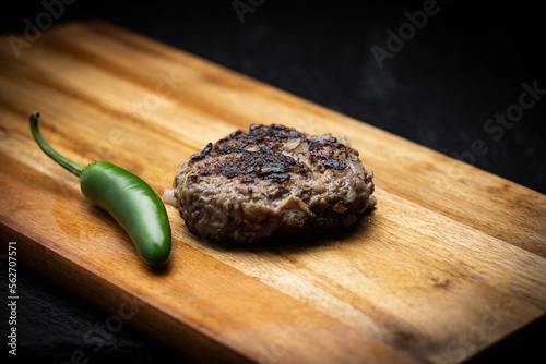 Traditional Bulgarian ground meat patty called kufte on wooden surface next to green chili pepper photo