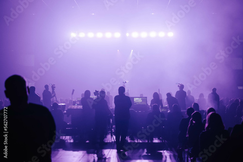 Concert of a musical rock band. Stage, fans, equipment, cameras in neon, purple light. Silhouette frame in backlight. Performance.