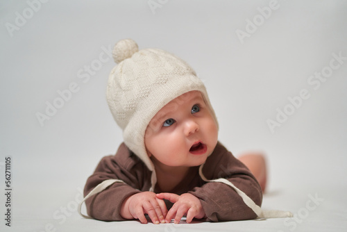 portrait of a keen infant on a light background in a warm knitted white hat