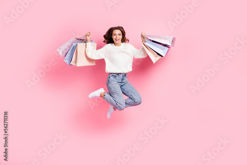Full length photo of excited lucky lady wear white sweater jumping rising shoppers isolated pink color background